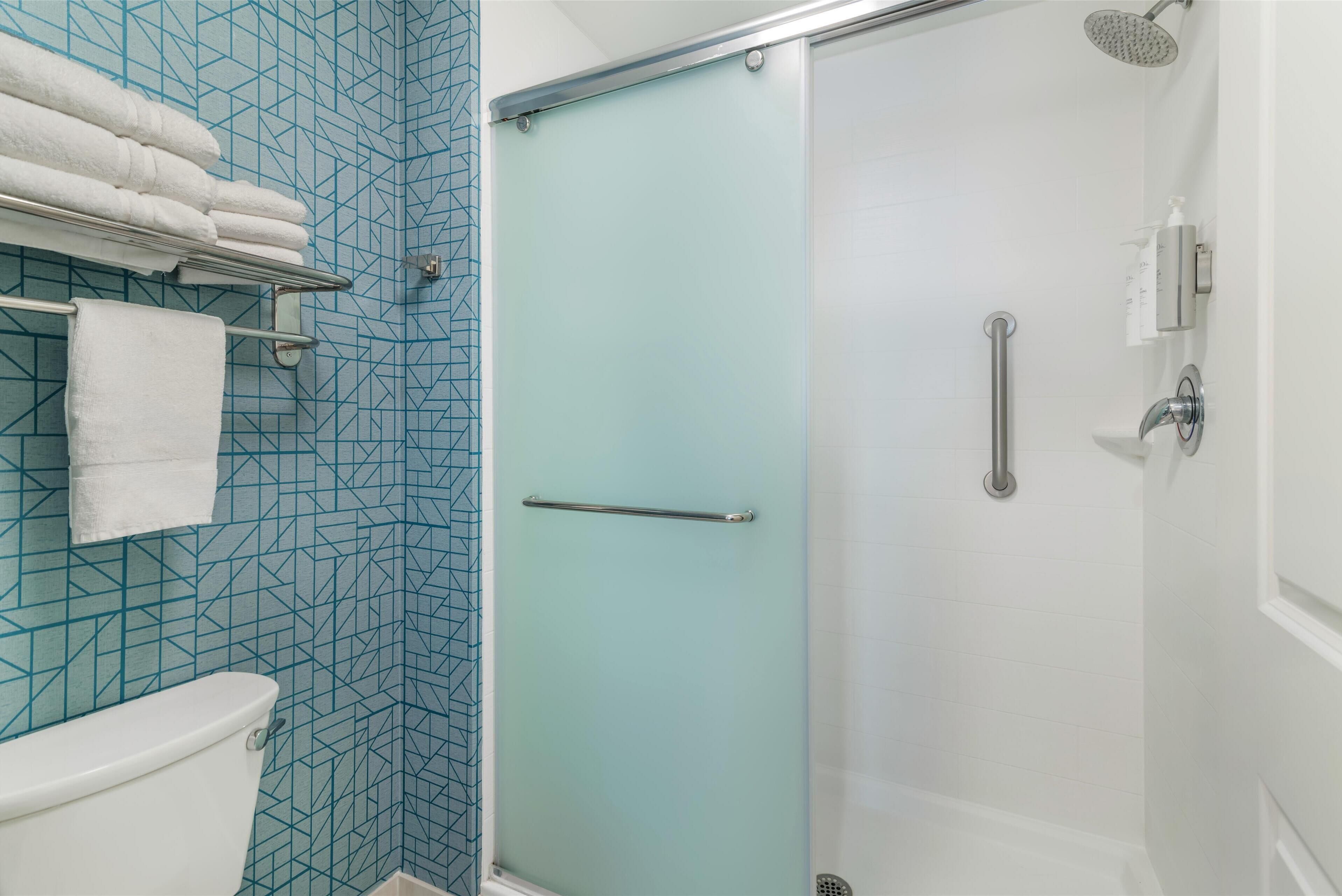 A bathroom with a toilet, a glass shower enclosure, and a towel rack with folded towels.