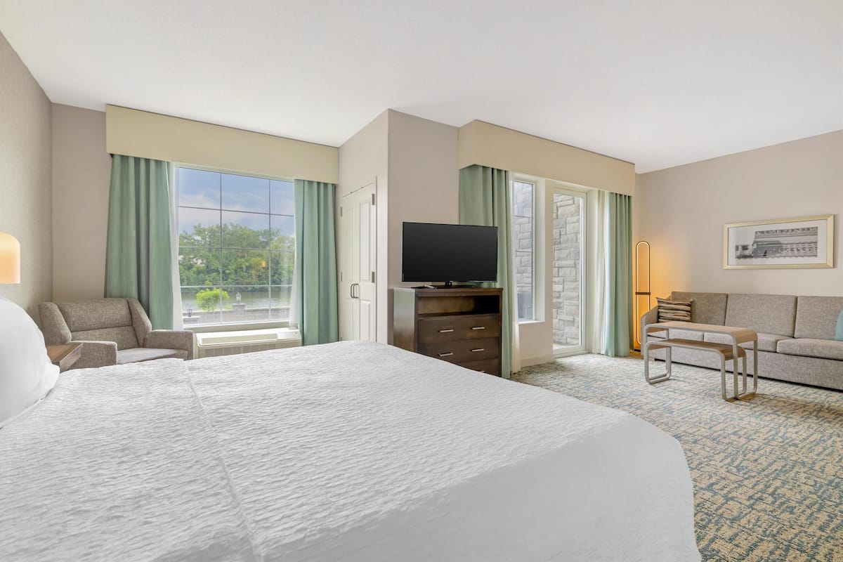 A hotel room with a large bed, a flat-screen TV, a sofa, and a dining table.