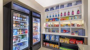 A vending area with two refrigerated beverage dispensers labeled 'COLD' and 'COLDER', and shelves stocked with snacks and beverages. - Homewood Suites By Hilton Schenectady (Schenectady)