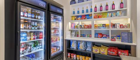 A vending area with two refrigerated beverage dispensers labeled 'COLD' and 'COLDER', and shelves stocked with snacks and beverages.