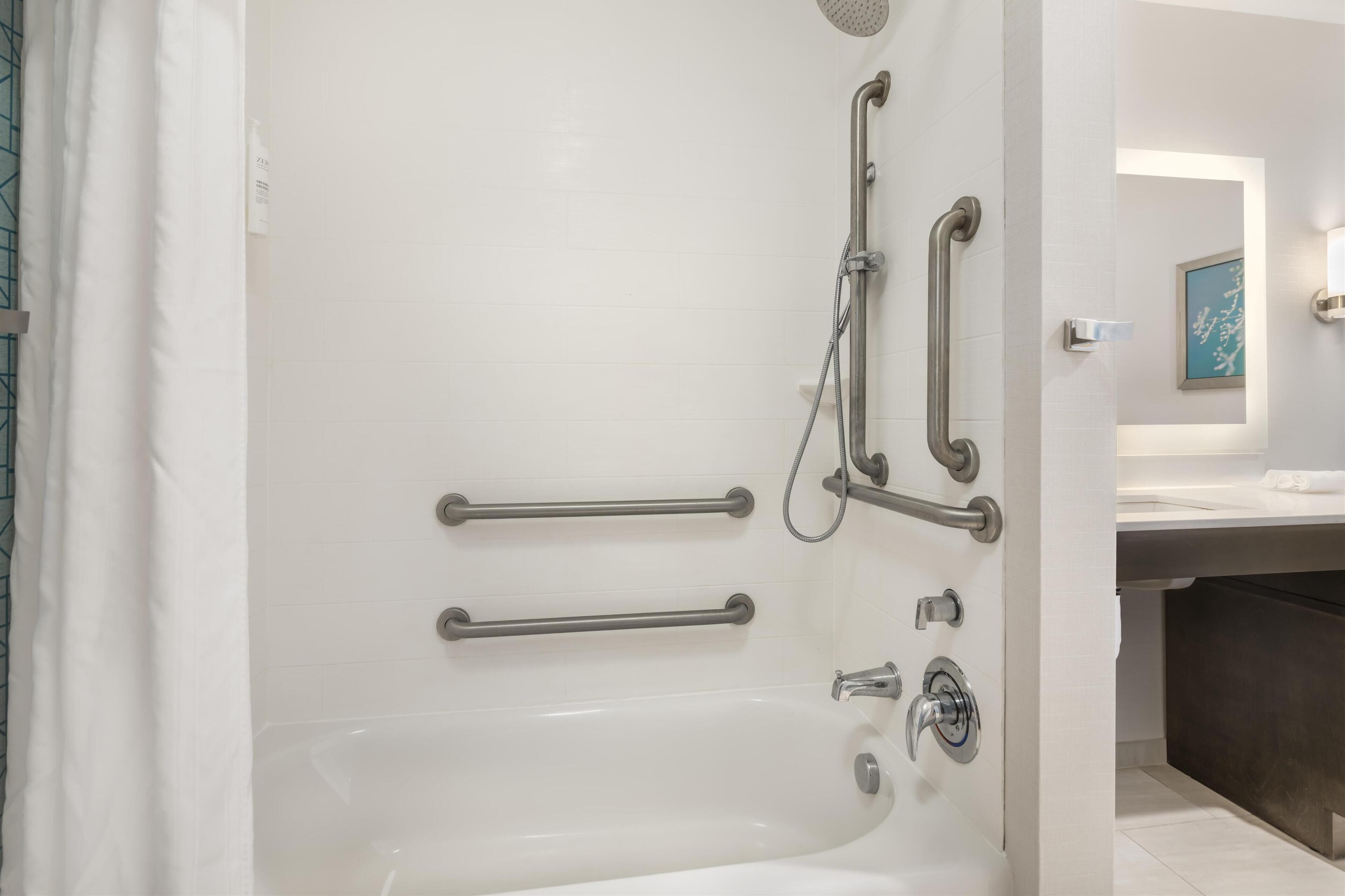 Un baño moderno con bañera, barras de apoyo y cabezal de ducha.