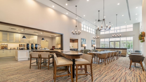 A spacious dining area with multiple tables and chairs, a kitchen in the background, and large windows allowing natural light. - Homewood Suites By Hilton Schenectady (Schenectady)