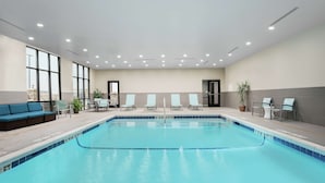 Une piscine intérieure à l’eau d’un bleu cristallin, entourée de chaises longues et d’un canapé.