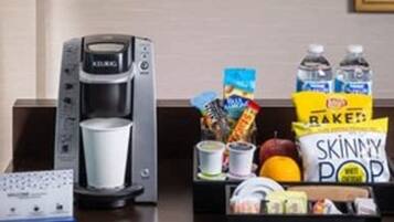 A kitchenette with a coffee maker, a kettle, a box of snacks, and a water bottle.