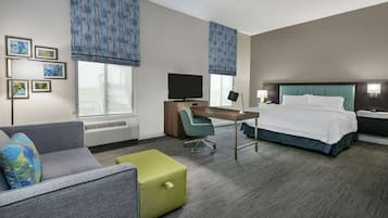 A hotel room with a bed, a desk, a chair, a sofa, and a small green ottoman.