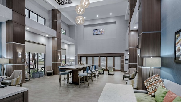Un hall d’entrée spacieux avec un bar central, des espaces aménagés pour s’asseoir et une grande fenêtre offrant une vue sur l’extérieur.