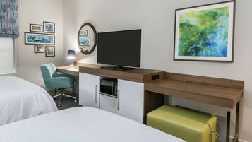 A hotel room with two beds, a desk with a flat-screen TV, a microwave, and a green ottoman.