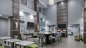 Un hall d’hôtel moderne doté d’un bar central, de nombreux espaces pour s’asseoir et d’un mélange de panneaux muraux en bois et de couleur grise.