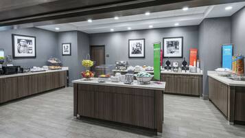 A modern hotel lobby with a central reception desk, a coffee station, and a refreshment area.