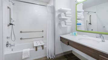 A modern bathroom with a walk-in shower, grab bars, a bathtub, a vanity with a mirror, and neatly stacked towels.