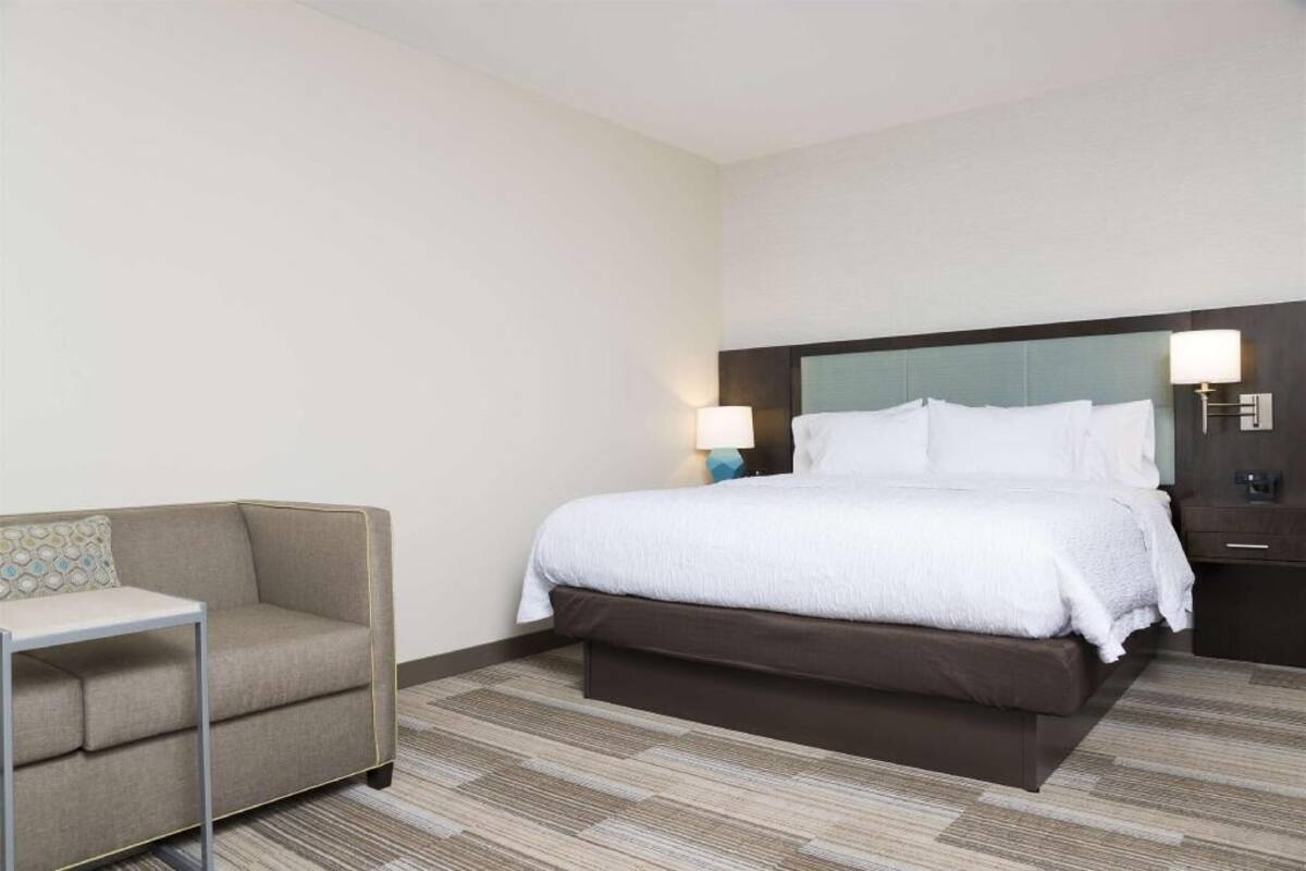 Quarto de hotel com cama, sofá, mesa de cabeceira e luminária.