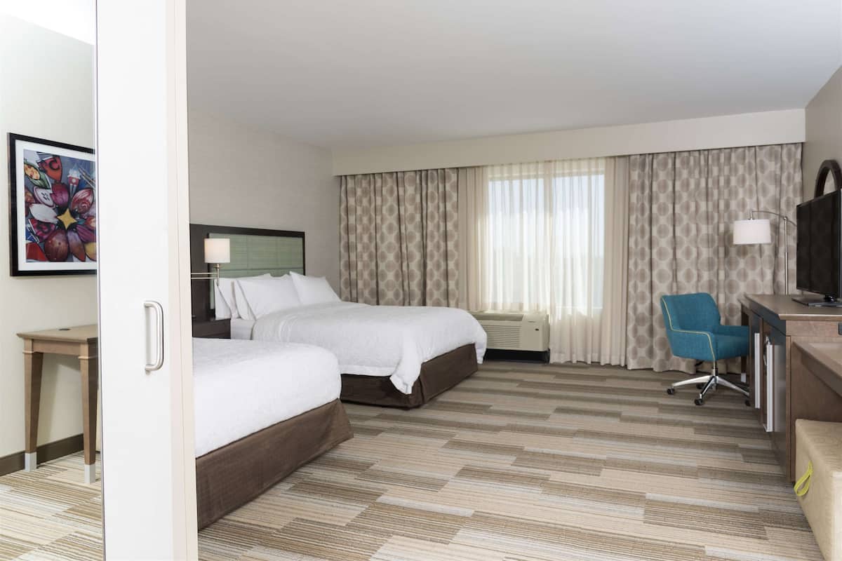 Quarto de hotel com duas camas, uma escrivaninha, uma cadeira e uma televisão.