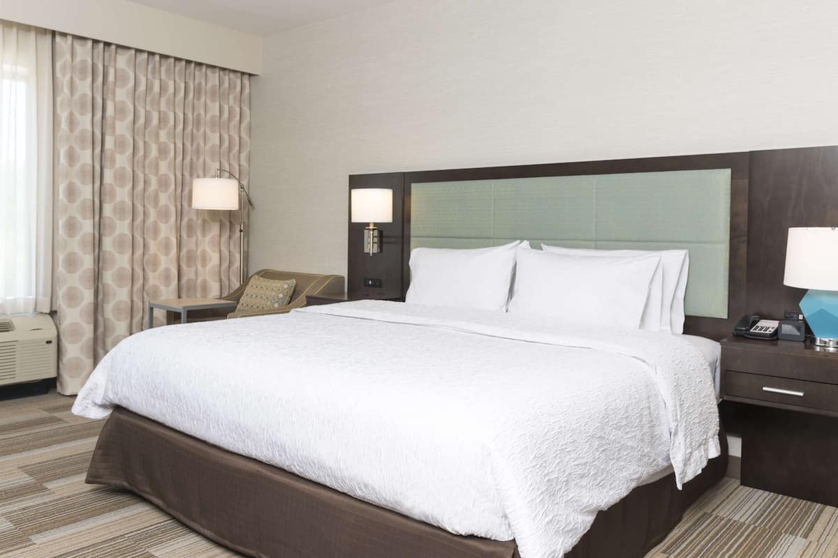 Quarto de hotel com uma cama grande, duas luminárias de cabeceira, mesa de cabeceira com telefone e janela com cortinas.