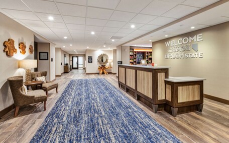 A hotel lobby with a blue carpet, wooden reception desk, and a welcome sign.