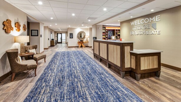 A hotel lobby with a blue carpet, wooden reception desk, and a welcome sign. - Hampton Inn & Suites Wells (Wells)