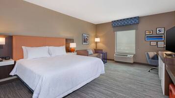 Quarto de hotel com uma cama grande, uma mesa de trabalho com cadeira, televisão e janela.