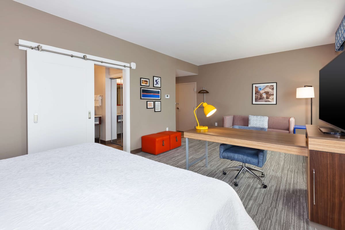 A hotel room with a bed, desk, chair, and a TV.
