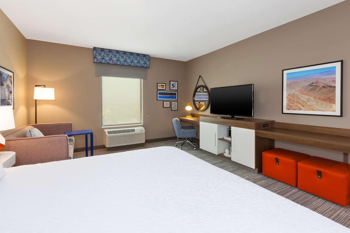 A hotel room with a bed, desk, chair, TV, and artwork on the walls.