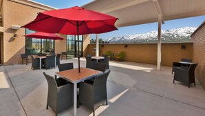 An outdoor patio with tables and chairs, red umbrellas, and a view of snow-capped mountains. - Hampton Inn & Suites Wells (Wells)