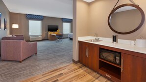 A modern hotel room with a kitchenette, a sofa, a desk, and a large window. - Hampton Inn & Suites Wells (Wells)