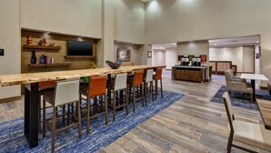 A modern hotel lobby with a long wooden reception desk, multiple seating areas, and a large TV mounted on the wall. - Hampton Inn & Suites Wells (Wells)