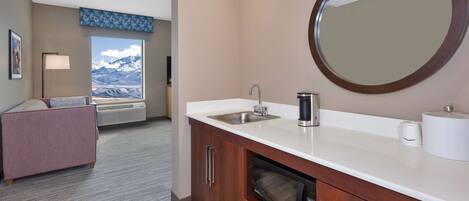 A modern bathroom with a sink, mirror, and coffee maker.