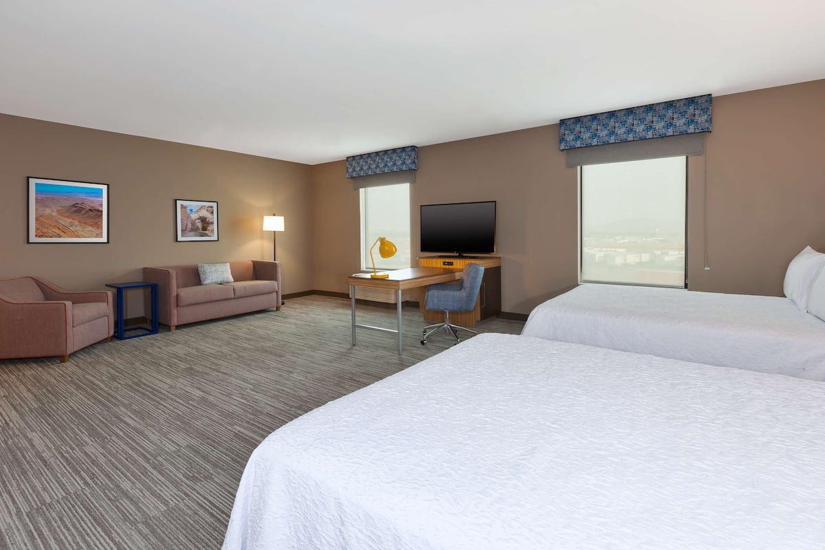 A hotel room with two beds, a desk, a chair, a TV, and two framed pictures on the wall.