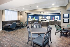 A modern hotel lobby with a dining area, sofas, and a kitchen counter. - Hampton Inn Kennebunk Kennebunkport (Kennebunk)