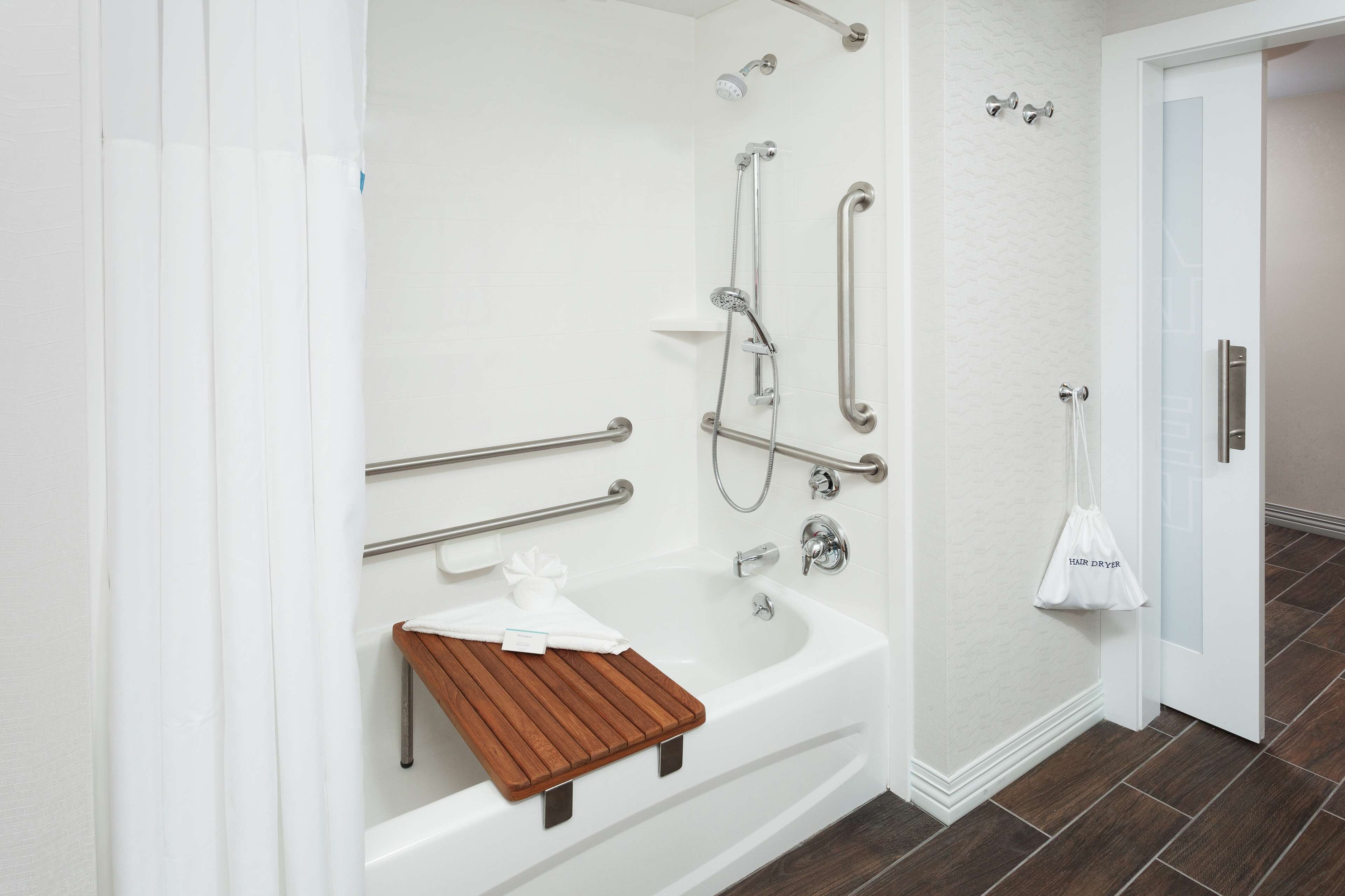 A modern bathroom with a bathtub, shower, and handrails.