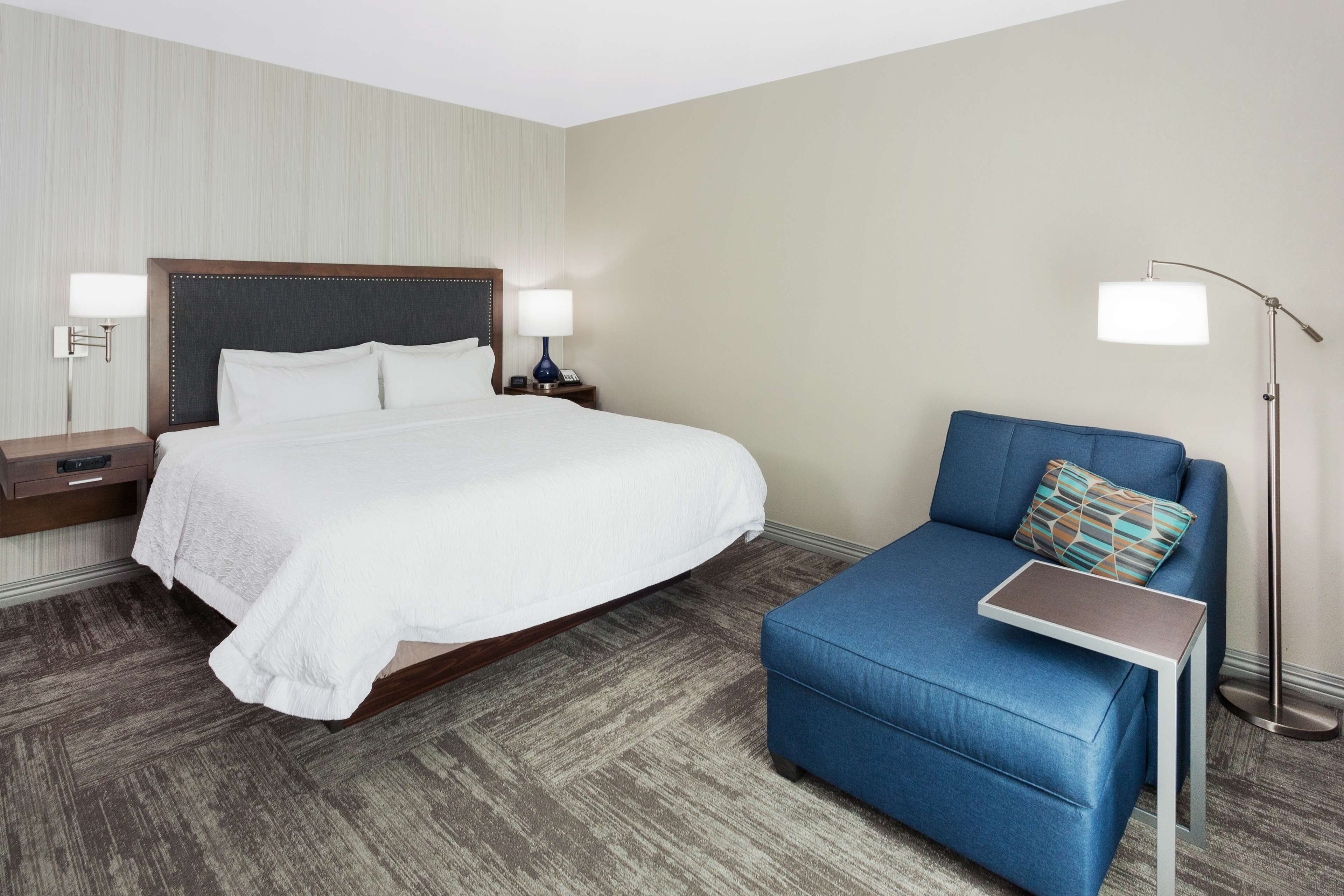 A hotel room with a large bed, a blue sofa, a small table, and a floor lamp.
