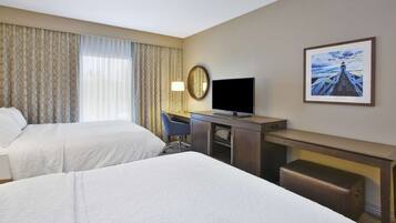 Una habitación de hotel con dos camas, un escritorio, una silla, un televisor, un espejo y un cuadro en la pared.