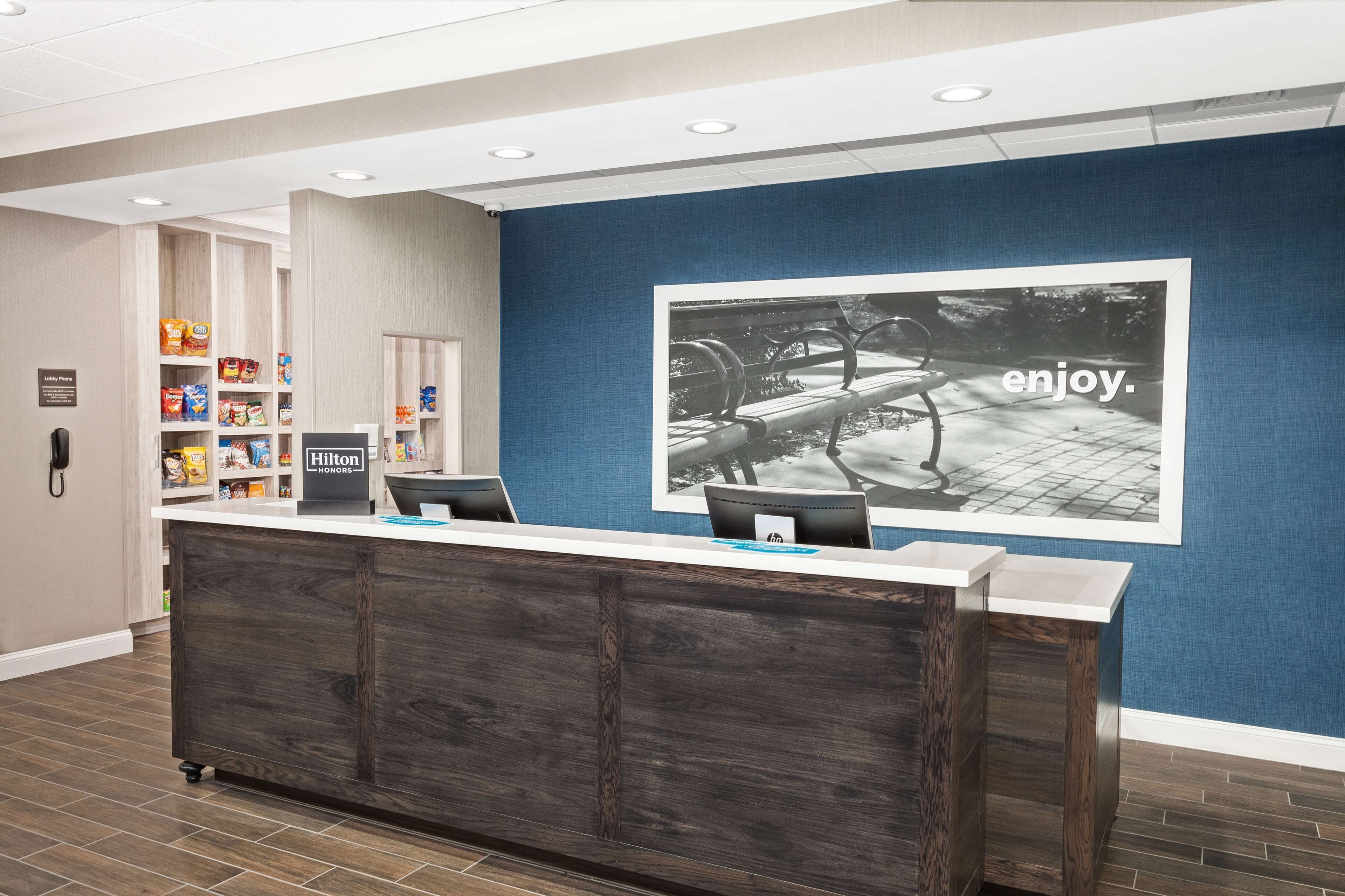 A reception area with a wooden reception desk, a blue wall with a large photo, and shelves stocked with snacks and toiletries.