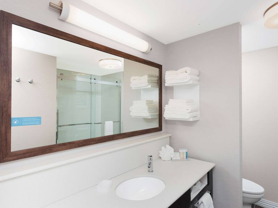 Un baño moderno con un espejo grande, lavamanos blanco y toallas ordenadas.