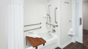 A modern bathroom with a bathtub, shower, and handrails.