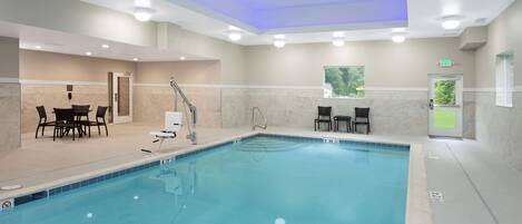 A swimming pool with a changing room, a table with chairs, and a window with a view of greenery.