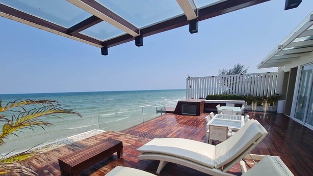 Une terrasse en bois avec des chaises longues blanches et une table, donnant sur l’océan.