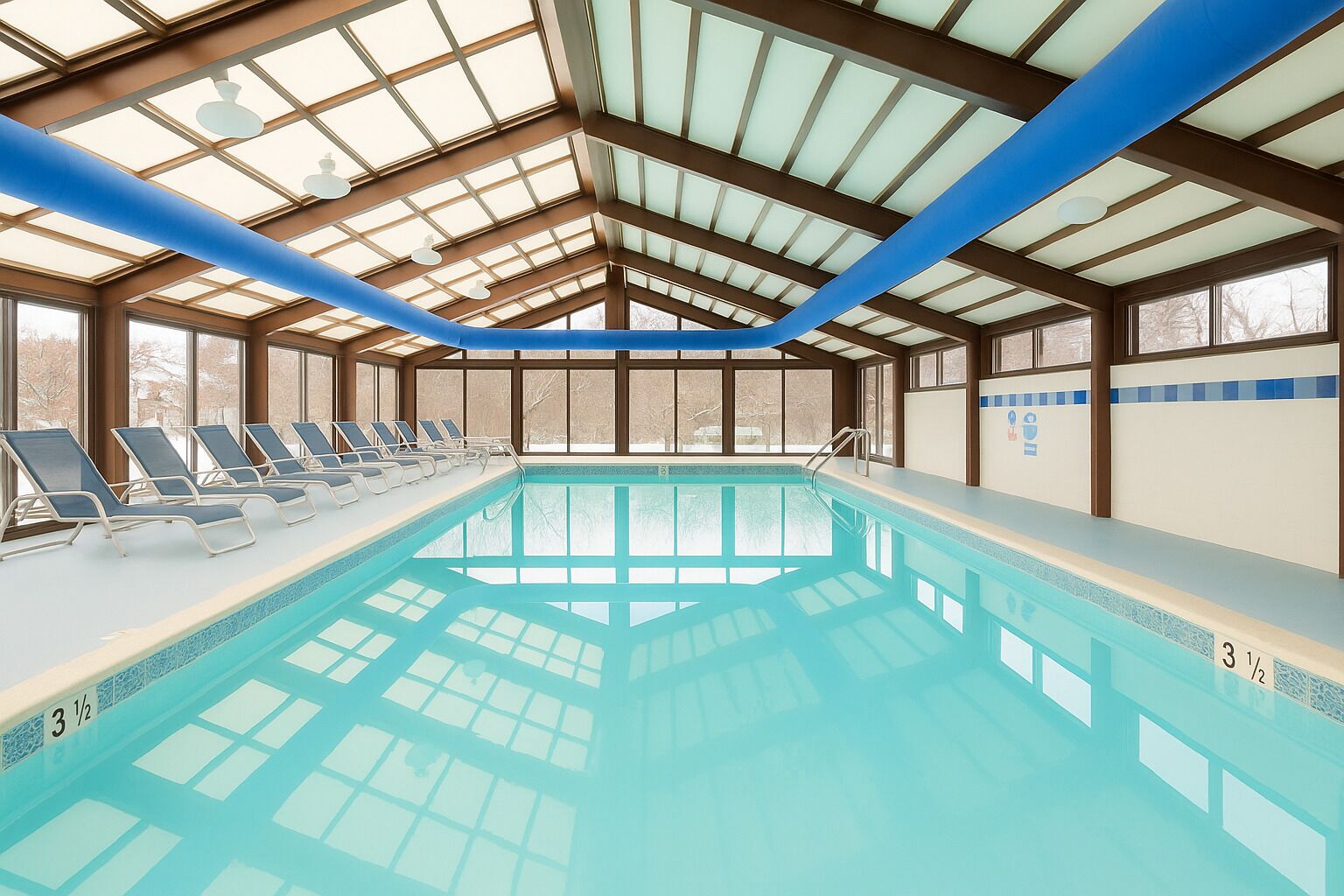 An indoor swimming pool with a clear roof structure, multiple lounge chairs, and a tiled pool edge.