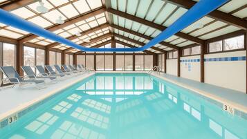 An indoor swimming pool with a clear roof structure, multiple lounge chairs, and a tiled pool edge.