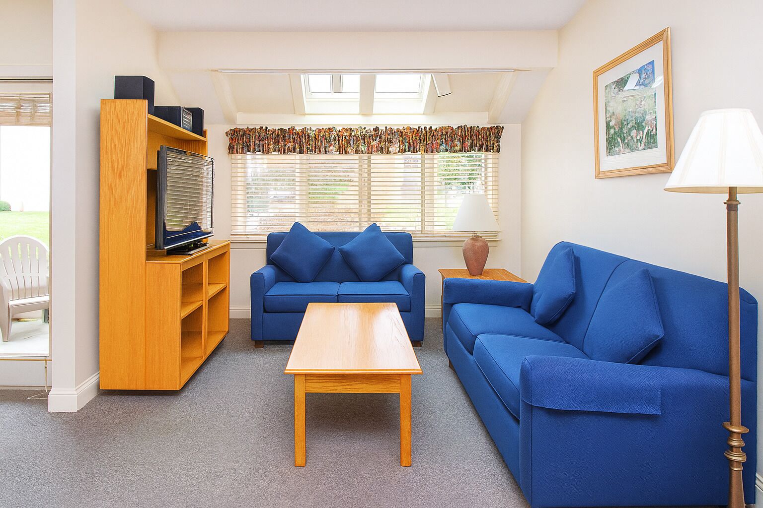 Een woonkamer met een blauwe zithoek, een houten salontafel en een boekenkast.