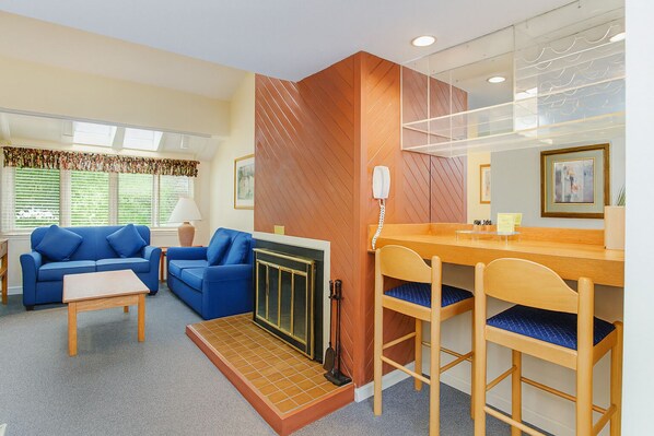 A cozy living room with a blue sofa, a wooden coffee table, and a fireplace. There is a dining area with a wooden table and chairs.
