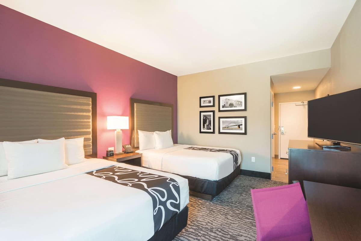 A hotel room with two beds, a TV, and a desk.