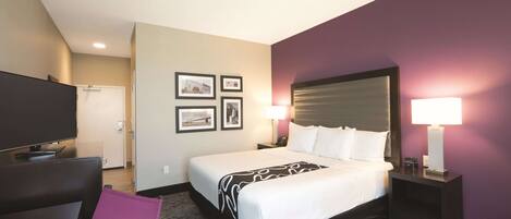 A hotel room with a bed, bedside tables, a TV, and framed pictures on the wall.