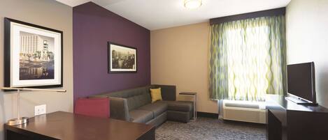 Une chambre d’hôtel équipée d’un bureau, d’un canapé, d’un tableau représentant un paysage urbain encadré, d’une fenêtre avec des rideaux et d’un téléviseur à écran plat.