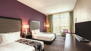 A hotel room with two beds, a desk, a TV, and a window with curtains.