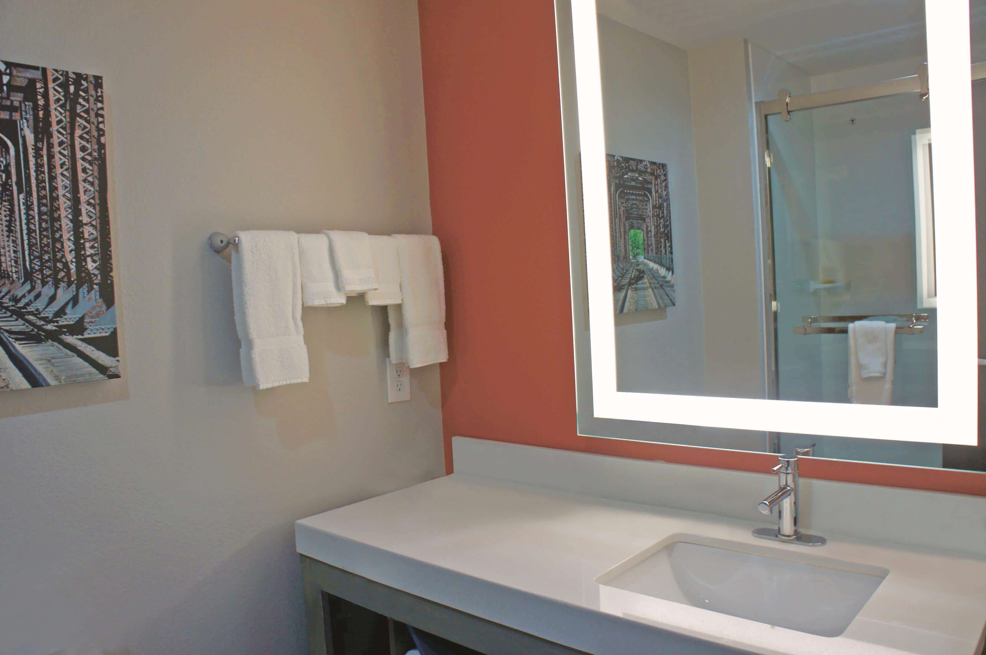 A bathroom with a white sink, a large mirror, and two white towels hanging on the wall.