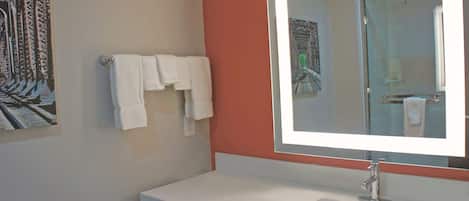 A bathroom with a white sink, a large mirror, and two white towels hanging on the wall.