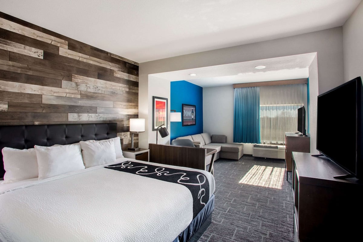 A hotel room with a large bed, a desk, a TV, and a seating area with a view of the outdoors.