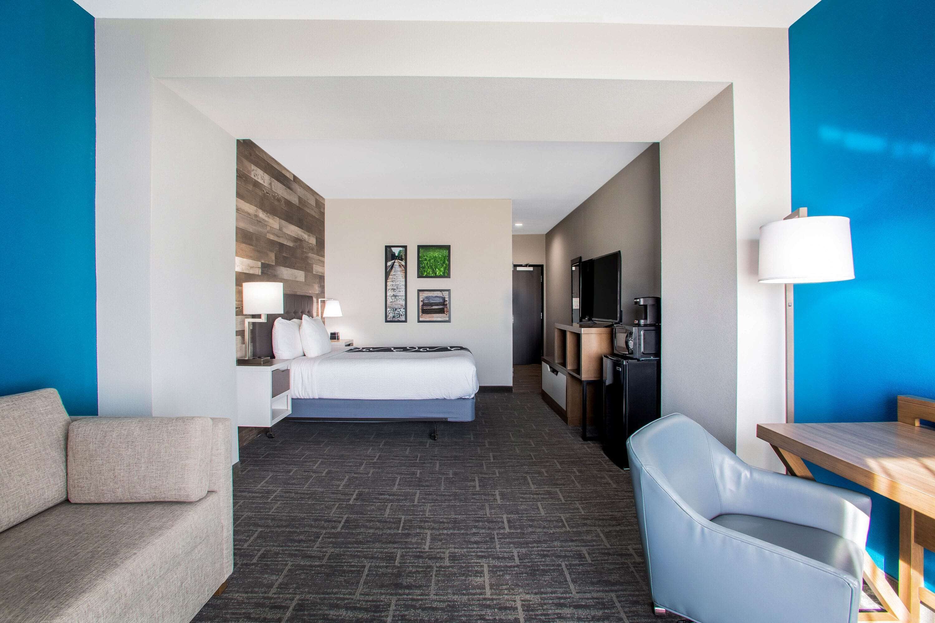 A hotel room with a bed, a desk, a chair, a TV, and a wall with a wooden panel design.