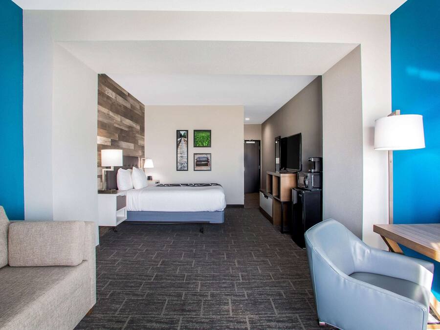A hotel room with a bed, a desk, a chair, a TV, and a wall with a wooden panel design.