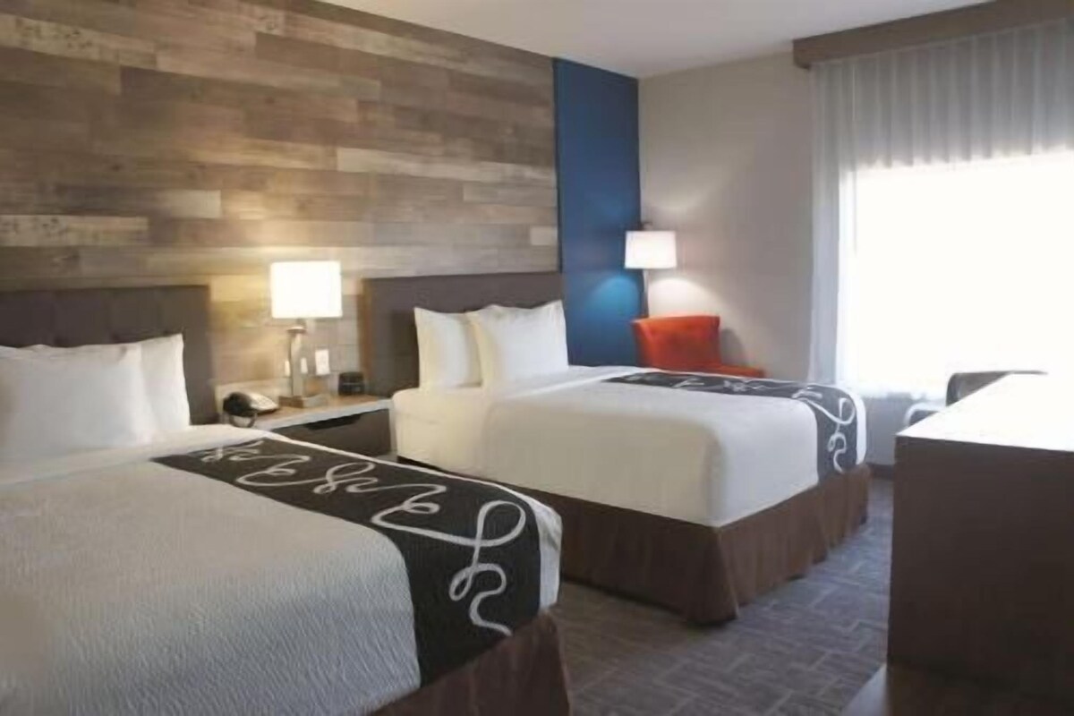 A hotel room with two beds, a desk, a lamp, and a window with curtains.
